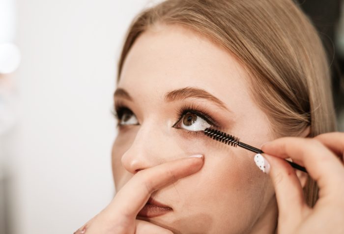 makeup artist applies mascara to lashes on a beautiful young woman blonde model, face make up